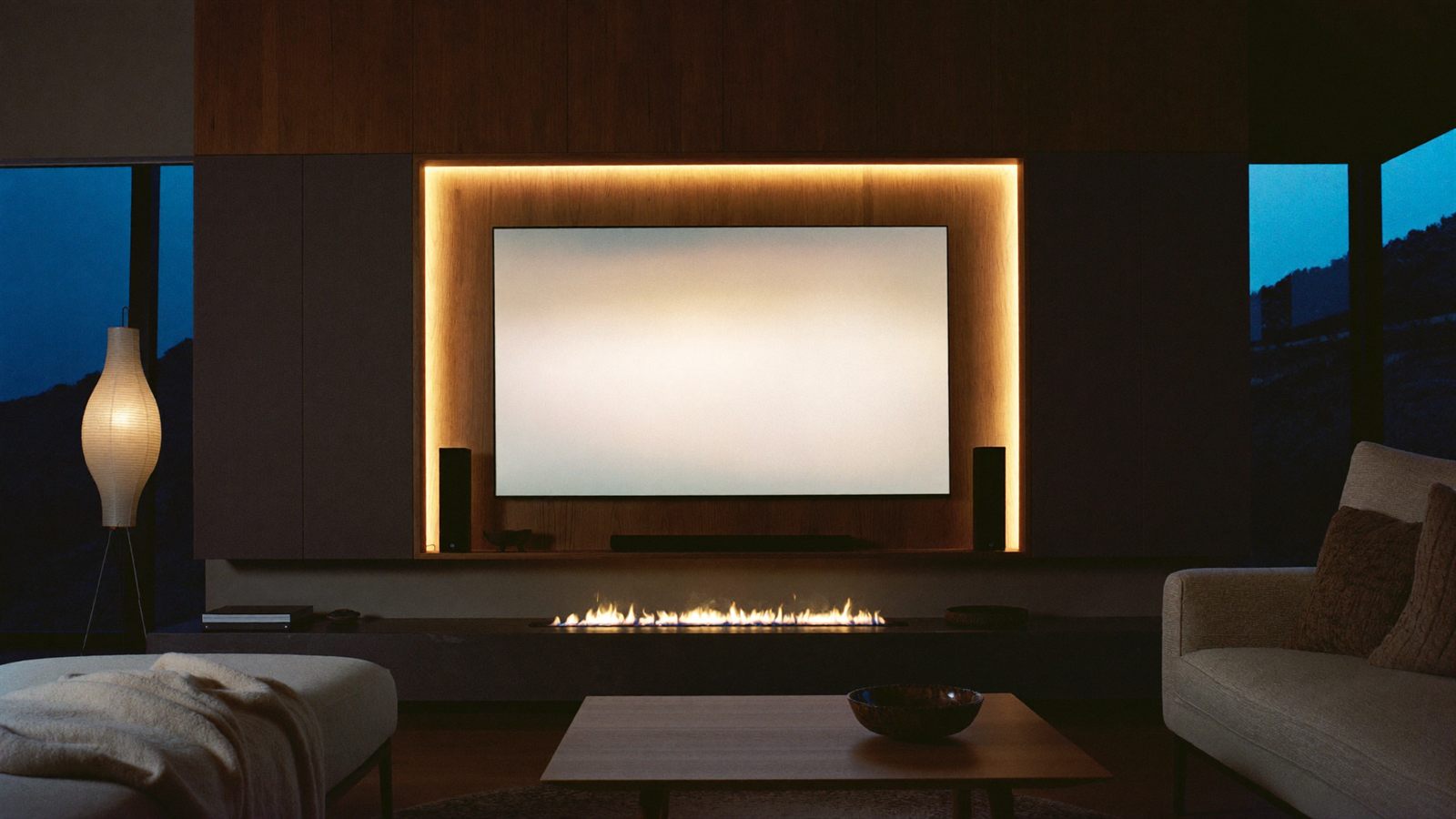 A modern lounge at night — a floating media wall with a soft halo of light glowing behind the screen
