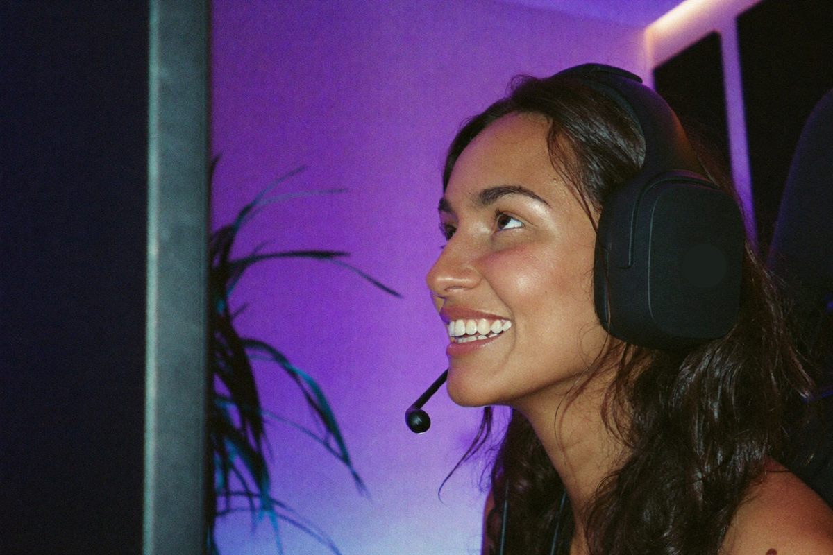 A player in a high-backed chair lit by shifting violet and cyan ambient light in a modern gaming den